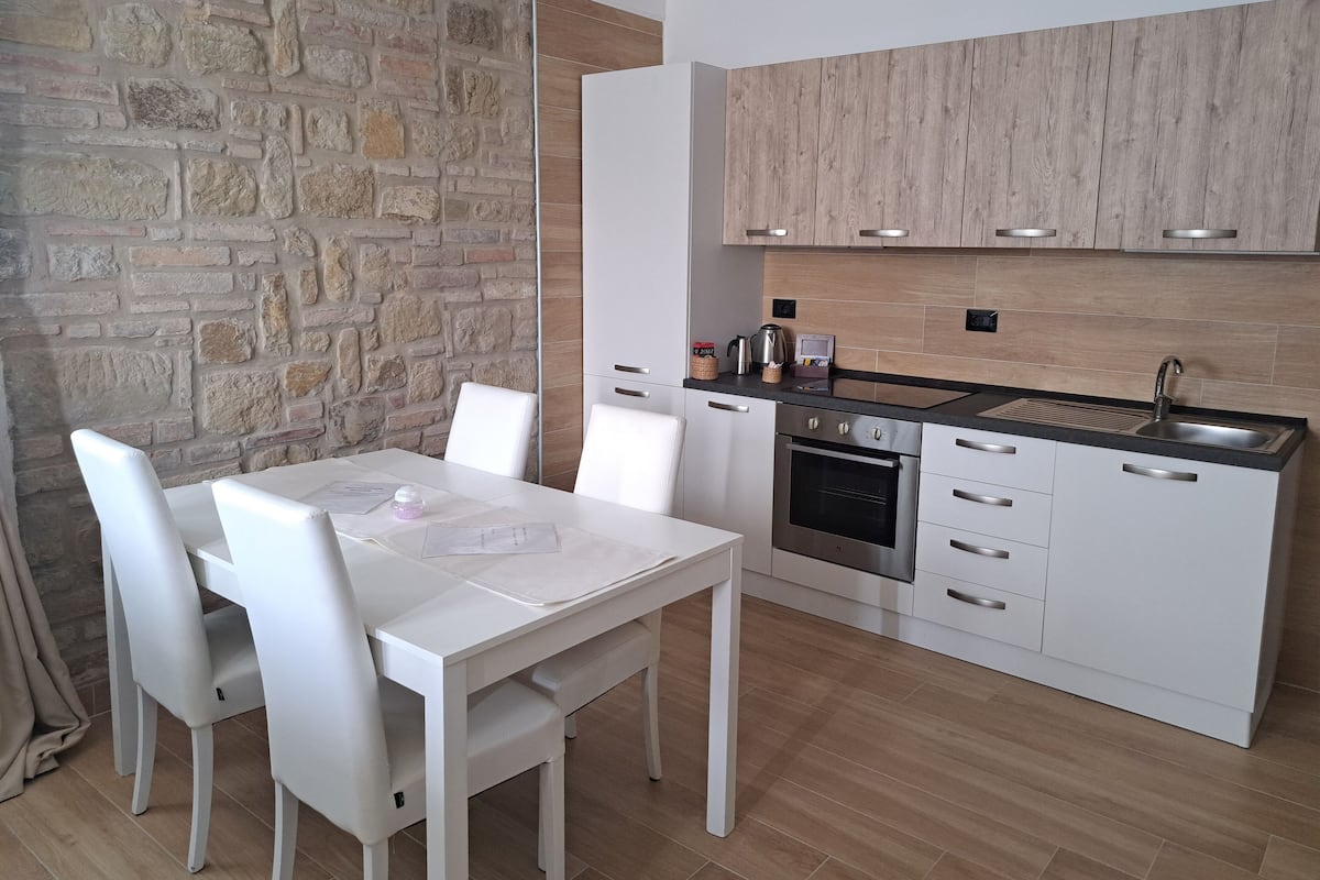 A modern kitchen with white cabinetry, a built-in oven, and a stone wall.