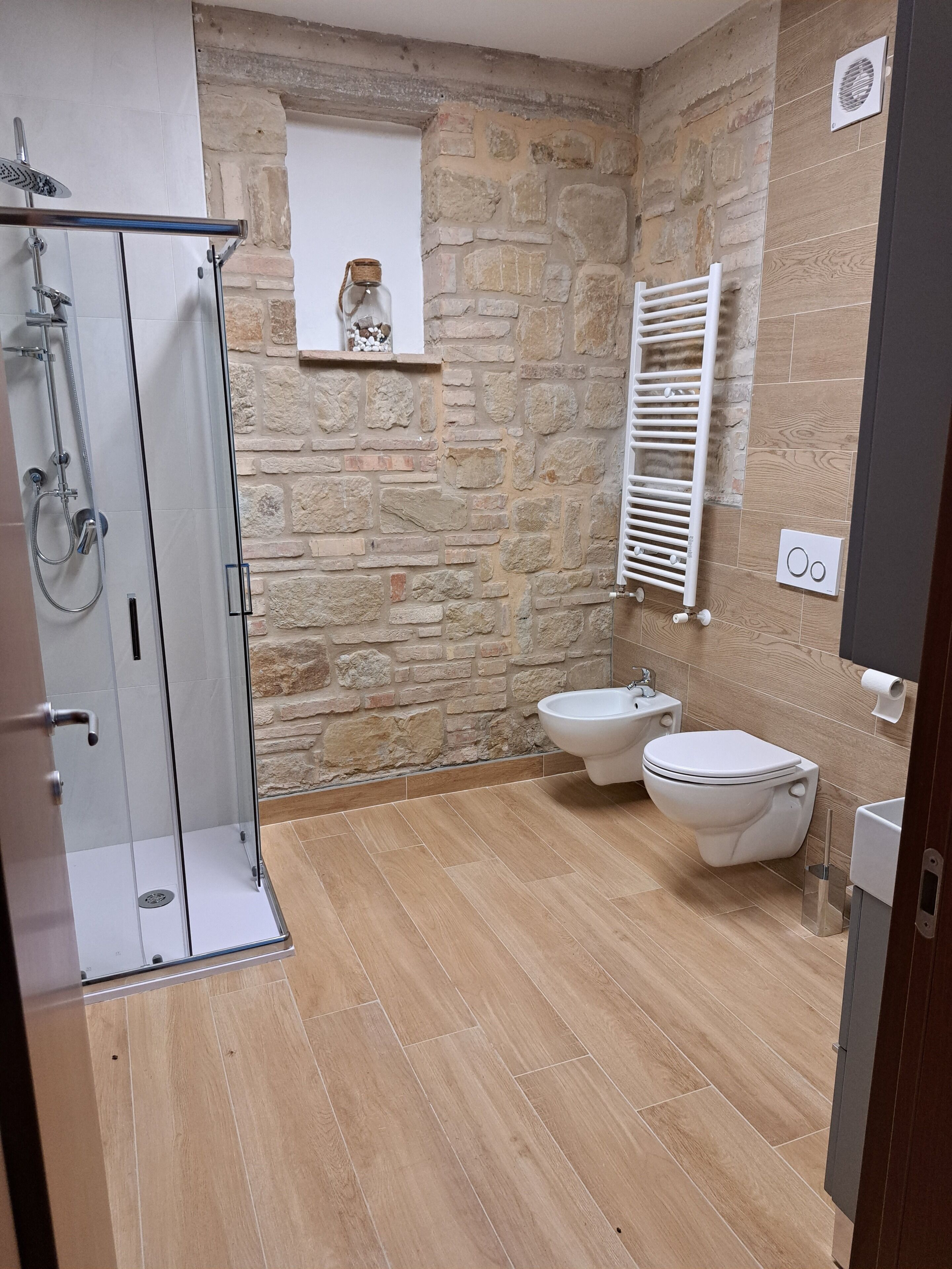 Un baño con ducha, inodoro, bidé y pared de piedra.