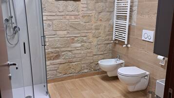 Un baño con ducha, inodoro, bidé y pared de piedra.