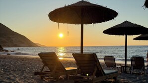 A beach with wooden lounge chairs and thatched umbrellas under a sunset. - Villa Yimaré / NEW 2024 Luxury villa / Private pool / Breathtaking sea views (Paralia Fodele)
