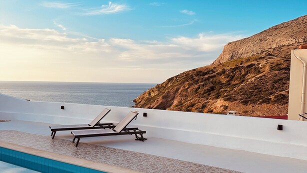 A pool area with lounge chairs and a view of the sea and a rocky hillside. - Villa Yimaré / NEW 2024 Luxury villa / Private pool / Breathtaking sea views (Paralia Fodele)