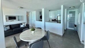 A modern living space with a dining area, a kitchen, and a seating area with a sofa and a TV mounted on the wall.