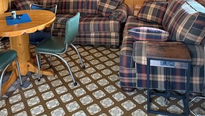 A cozy cabin interior with a plaid sofa, a small dining table, and a mirror reflecting a kitchen area.