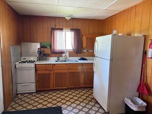 A compact kitchen with wooden cabinets, a gas stove, a refrigerator, and a patterned floor. - Family & Pet Friendly Lakefront Cabin - Five Mile Lake Lodge  (Chapleau)