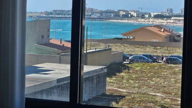 A view of a coastal area with buildings, a beach, and parked cars.