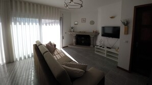 A living room with a sofa, a fireplace, a TV mounted on the wall, and a door leading to another room.