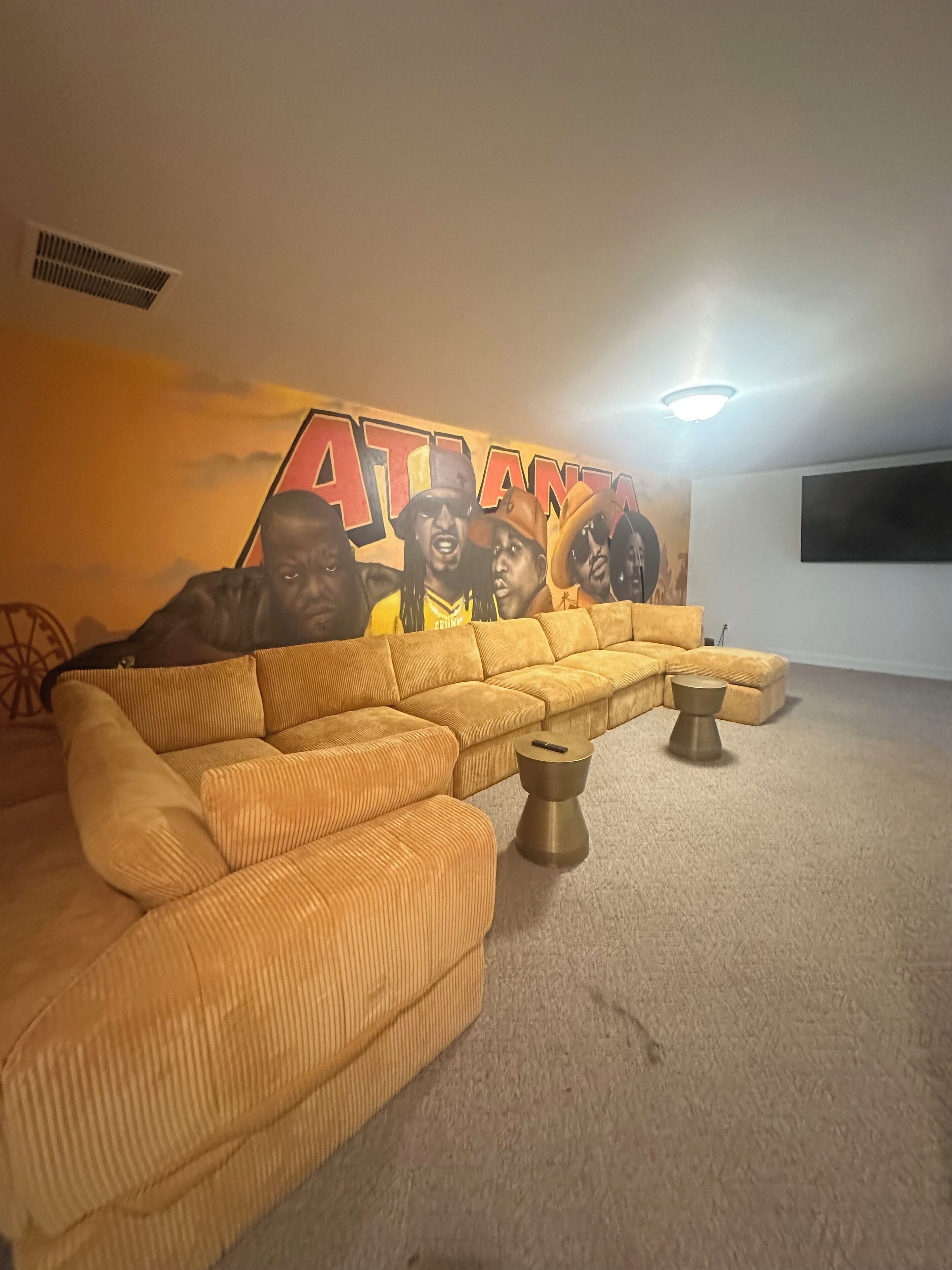 Una sala de estar con un amplio sofá modular, un mural en la pared y un televisor de pantalla plana.