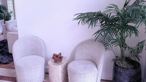 A room with two grey upholstered chairs, a small round side table with a woven texture, and a large potted plant with long green leaves. - STAR MANSION ATLANTA (Atlanta)