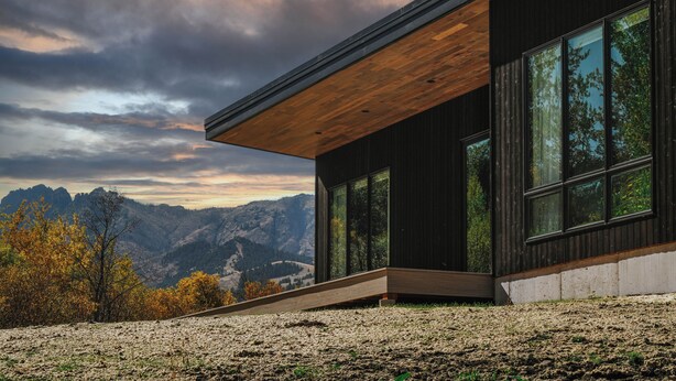 Un edificio moderno con amplios ventanales, techo de madera inclinado y vistas a montañas.