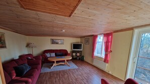A cozy living room with a wooden ceiling, a red sofa, a wooden coffee table, and a television. - Vacation apartment Fagerhult (Kalmar län)
