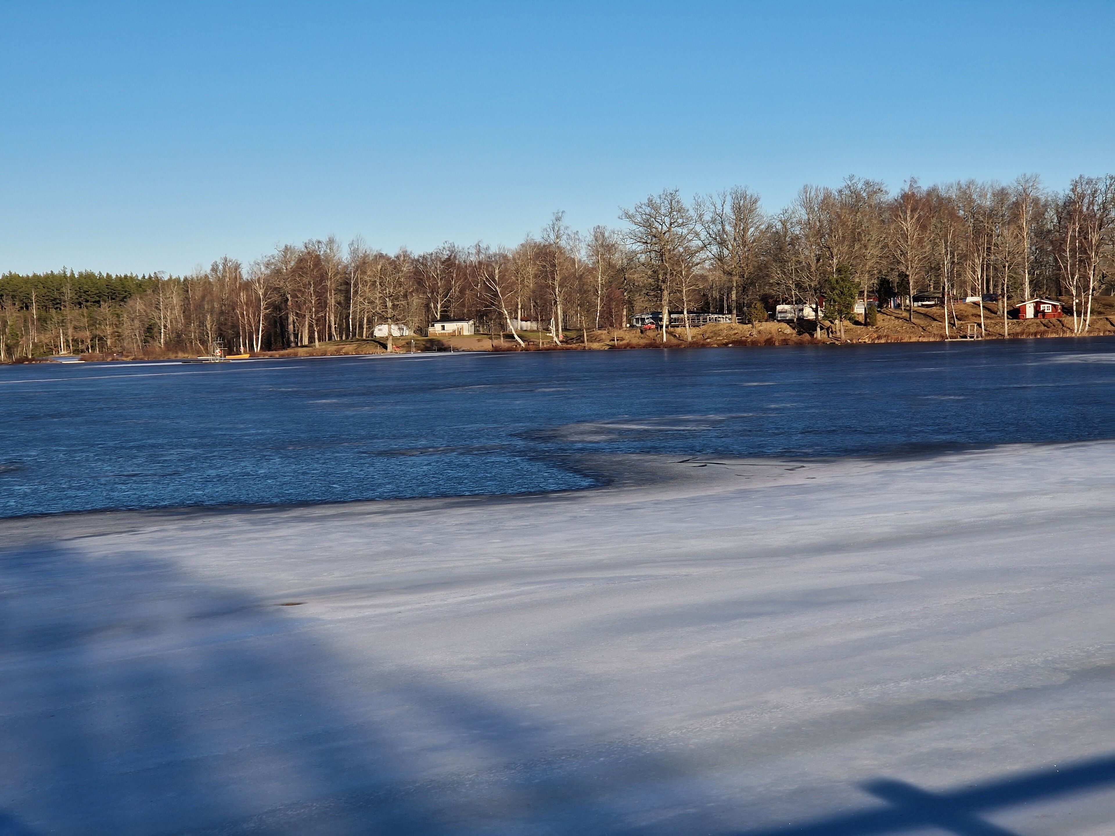 Un lac gelé, avec un ciel dégagé et des arbres sans feuilles en arrière-plan.