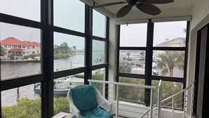 Un balcon donnant sur un port de plaisance, une chaise en osier blanche et un ventilateur de plafond.