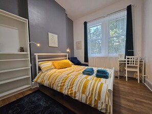 A bedroom with a bed, a desk, and a chair.