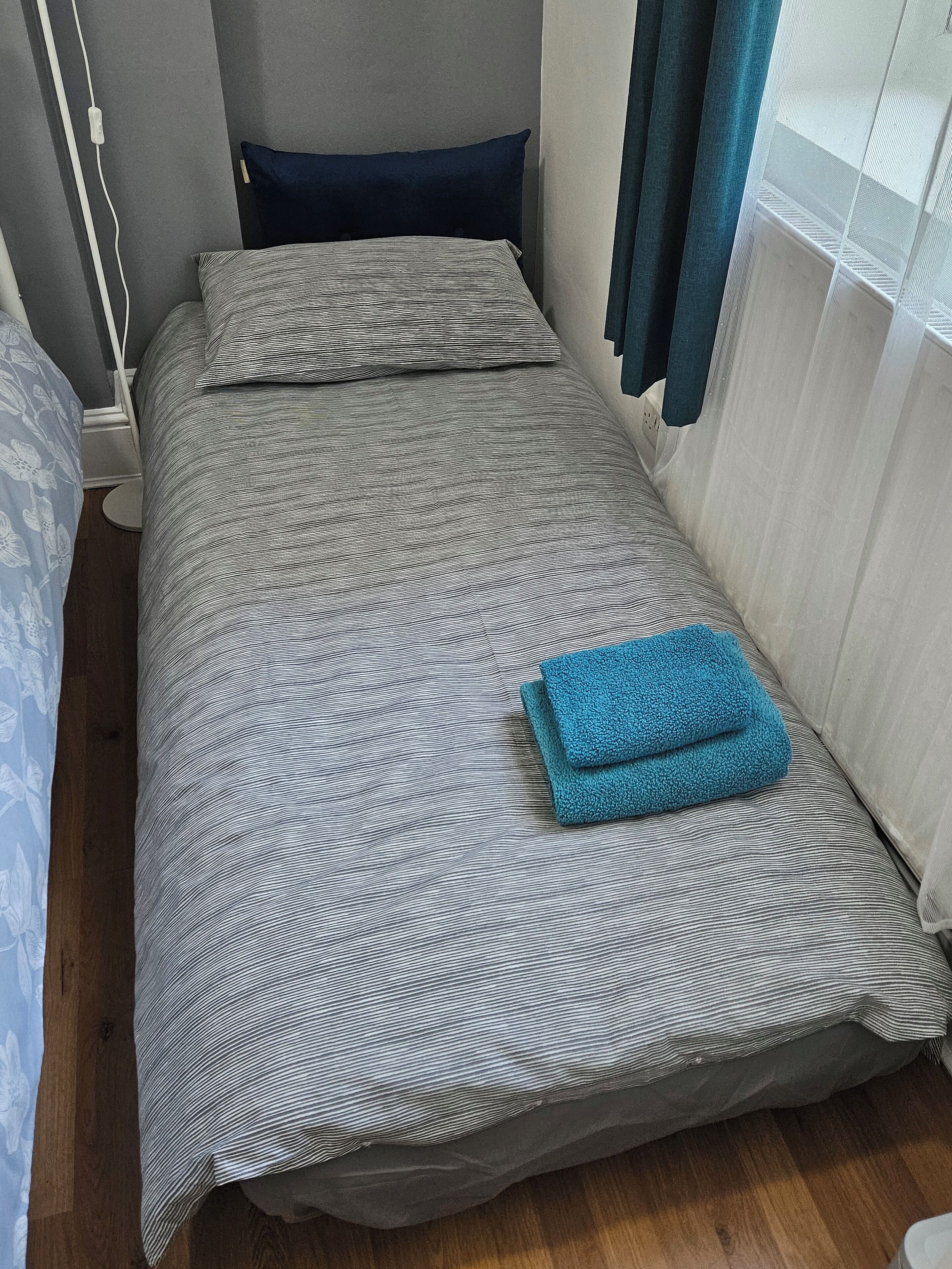 A small, single-bed room with a striped bedspread, a blue pillow, and a folded blue towel on the bed.