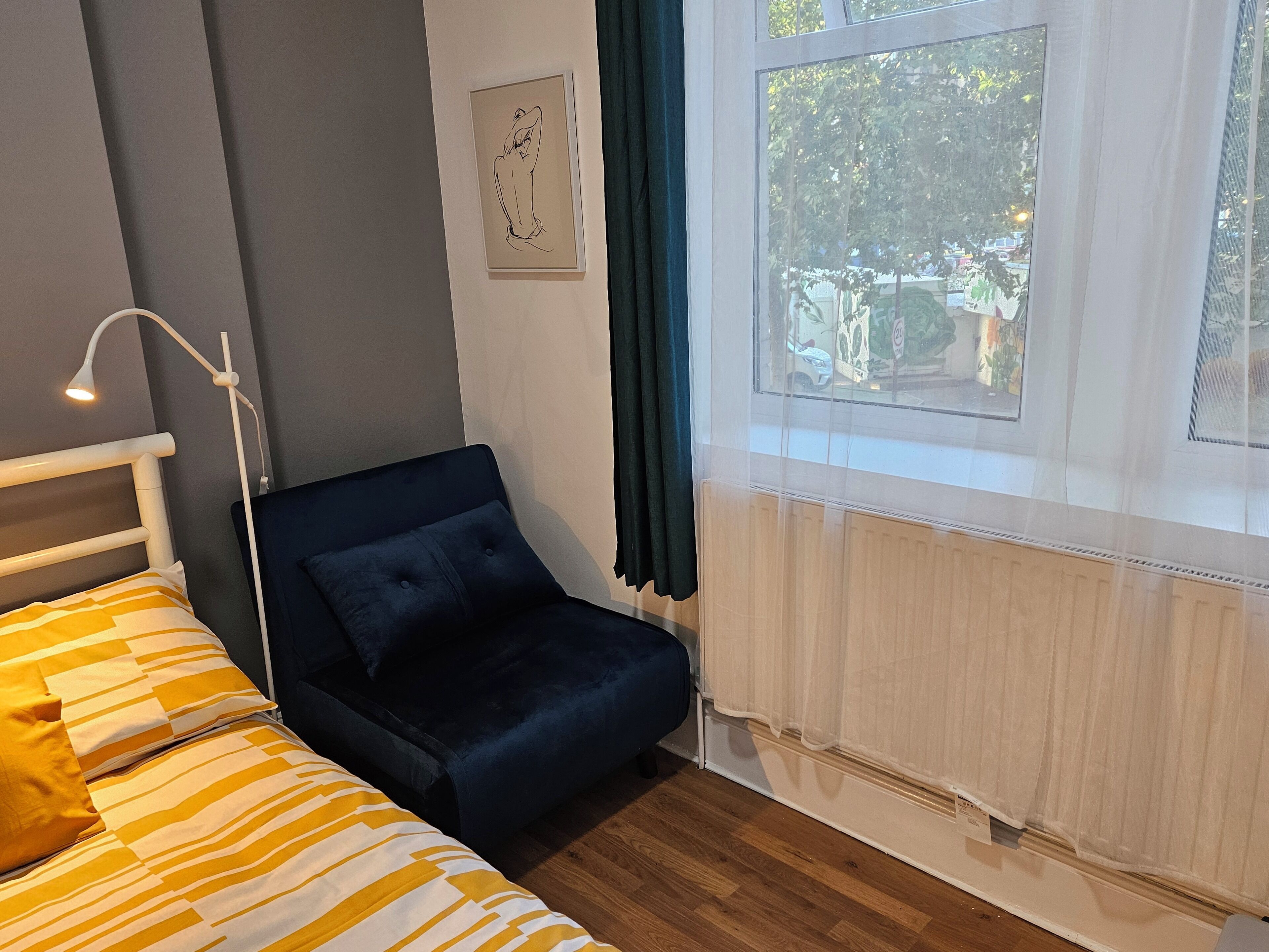 Ein Schlafzimmer mit Bett, Stuhl, Fenster und Heizkörper.