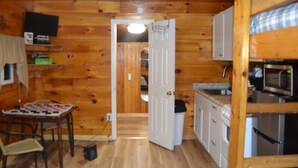 A wooden cabin interior with a kitchen area, a dining table with chairs, and a small television on a shelf. - Cozy & efficient cabin w/ river access. Pet Friendly! (Stanton)