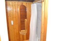 A wooden-paneled bathroom with a shower, a mirror, and a door. - Cozy & efficient cabin w/ river access. Pet Friendly! (Stanton)