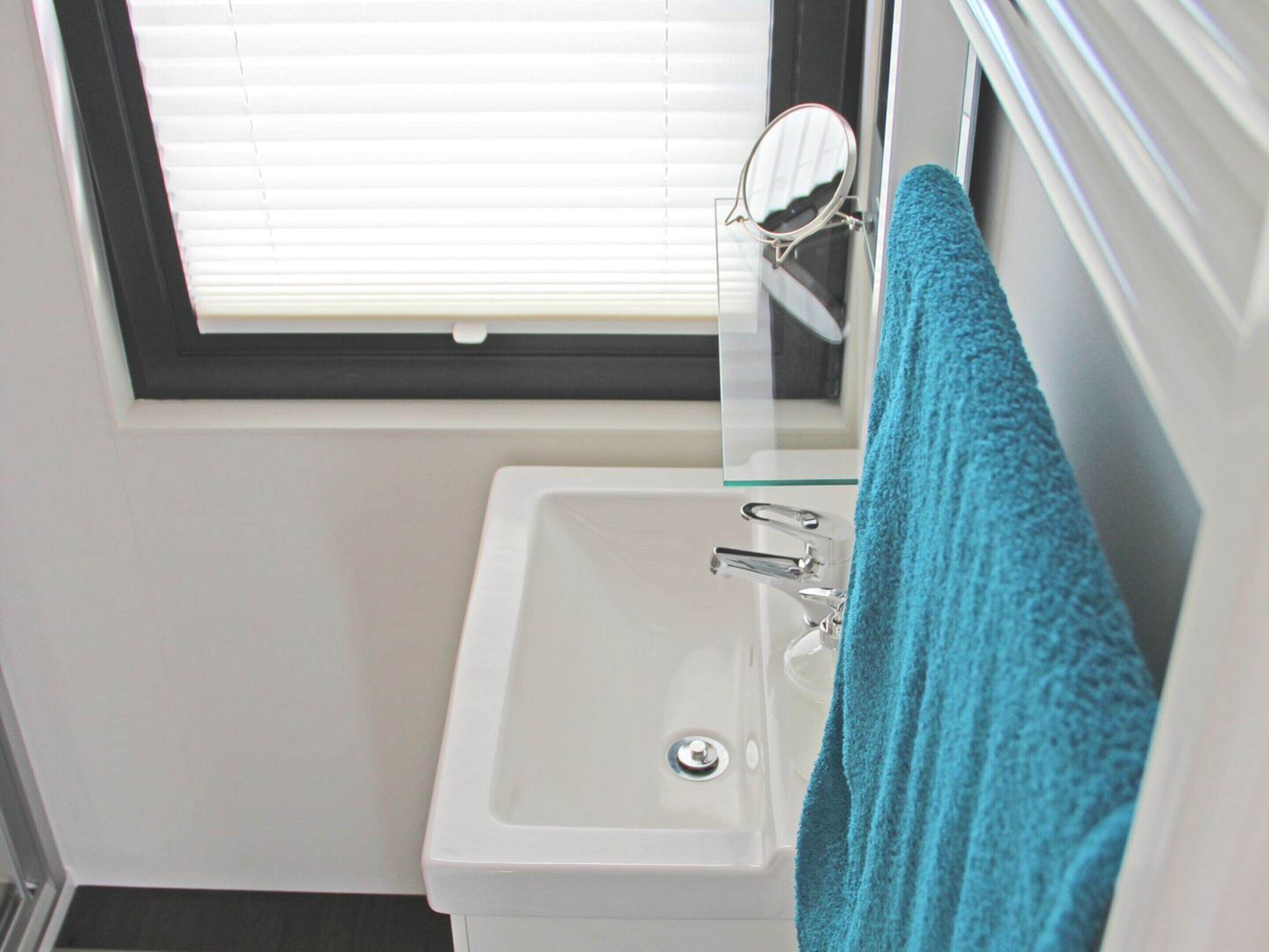 A small bathroom with a white sink, a mirror, and a window with blinds.