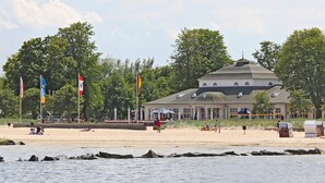 Ein Gebäude mit Kuppeldach in der Nähe eines Strandes, an dem Flaggen wehen und sich Menschen aufhalten.