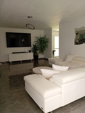 A modern living room with a large flat-screen TV, a white leather sofa, a potted plant, and a geometric wall decoration. - Villa in Valras-Plage, 700 m from the beach, with a heated indoor pool   (Valras-Plage)