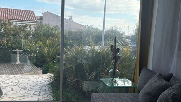 Een kamer met een grote schuifdeur die uitkomt op een patio met een stenen vloer, een glazen tafel en een bank met kussens.