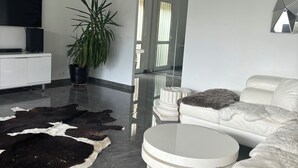 Een moderne woonkamer met een witte bank, een ronde salontafel, een grote potplant en een zwart-wit koeienhuidtapijt.