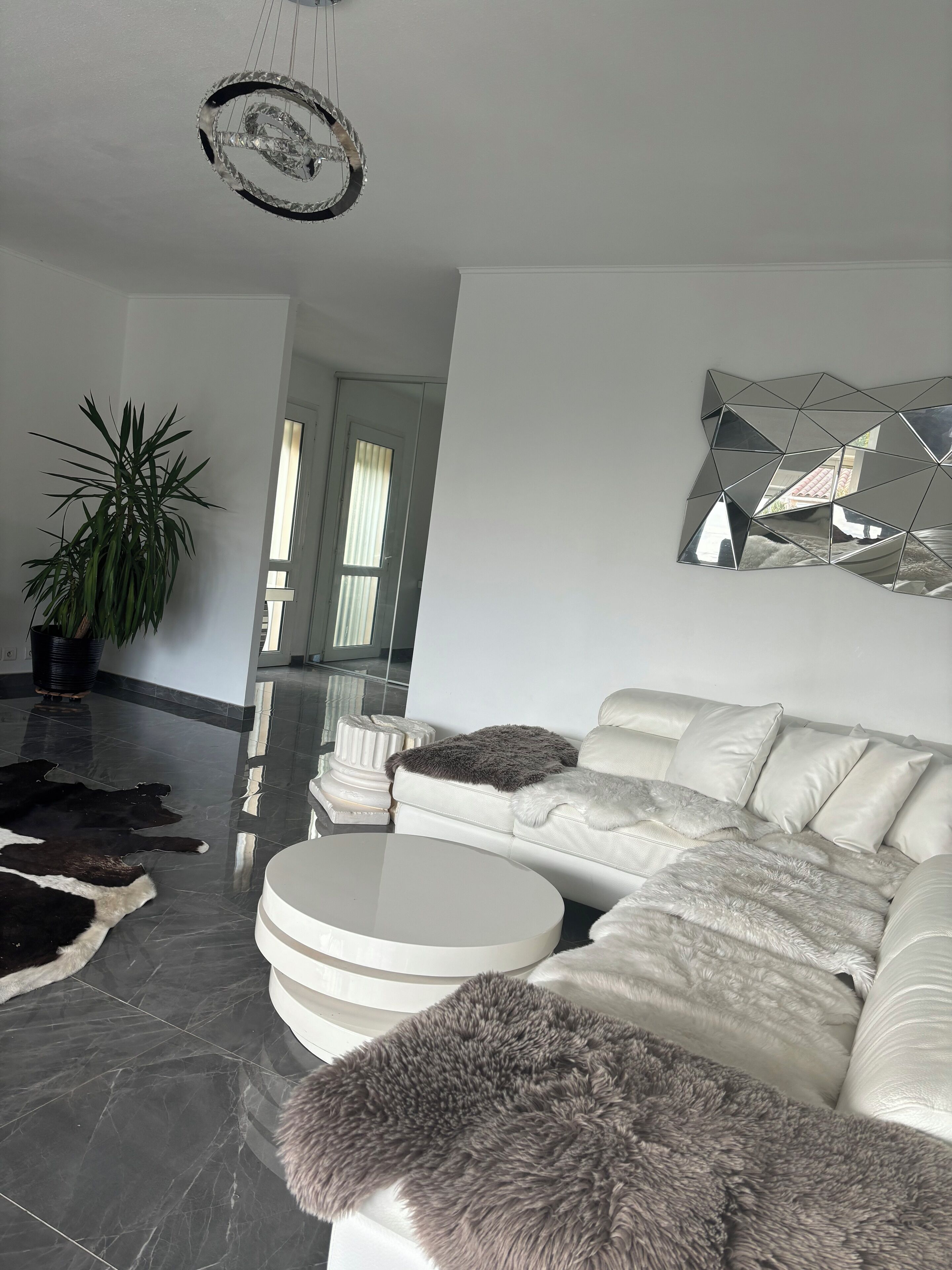 Een moderne woonkamer met een witte leren bank, een ronde salontafel en een grote abstracte spiegel aan de muur.