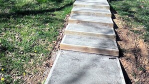 A concrete pathway leading to a house with a wooden deck and a covered area with a chair. - Barndominium getaway oasis! Close to Chattanooga shopping restaurants and Water! (Apison)