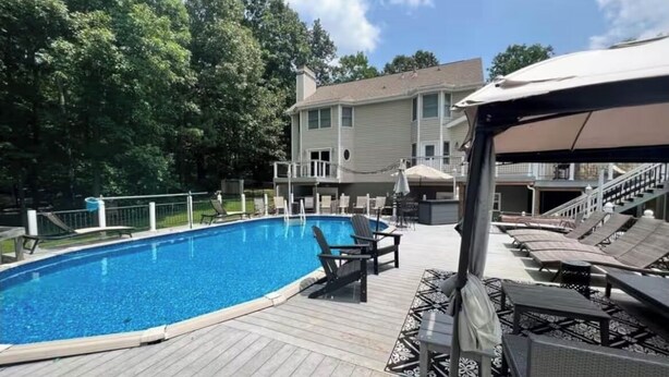 A swimming pool with lounge chairs and umbrellas, surrounded by a deck and trees. - Barndominium getaway oasis! Close to Chattanooga shopping restaurants and Water! (Apison)