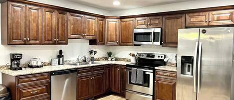 Cocina con armarios de madera, electrodomésticos de acero inoxidable y encimera de granito.