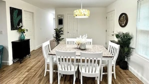 Een eethoek met een ronde tafel, witte stoelen, een hanglamp en een potplant.