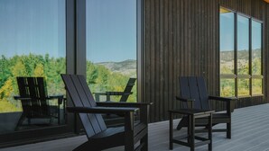 Eine Terrasse mit zwei Adirondack-Stühlen und einem Glastisch mit Blick auf eine bewaldete Landschaft.