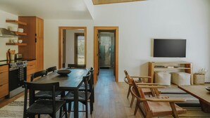 Eine moderne Küche mit Holdekor, ein Essbereich mit großem Tisch und Stühlen sowie ein an der Wand befestigter Fernseher.