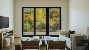 Ein modernes Wohnzimmer mit großem Fenster, Flachbildfernseher, Sofa und Esstisch.