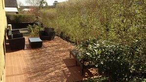 Un espace extérieur aménagé en patio, avec un sol en briques, des meubles de jardin noirs et un feuillage verdoyant et luxuriant.