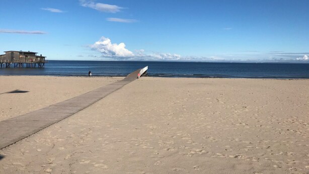 Une plage avec une promenade en béton menant à l’eau, une jetée et un ciel dégagé.