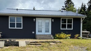Une maison de plain-pied à l’extérieur sombre, avec une porte d’entrée et deux fenêtres.
