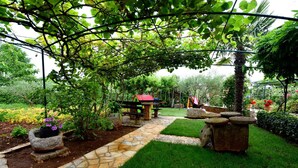 Un giardino con un sentiero in pietra, un tavolo da picnic in legno e una struttura con tetto rosso.