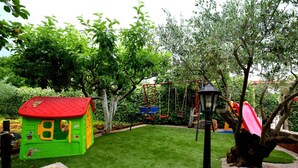 Un’area giochi per bambini con una piccola serra, altalene e uno scivolo.