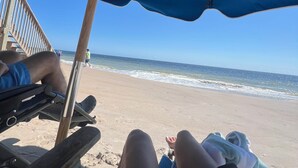 Eine Strandansicht mit einem Holzstuhl und einem Sonnenschirm.
