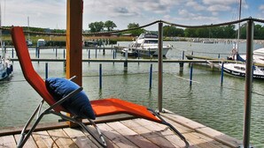 Una terraza de madera con una silla de descanso y vista a un puerto deportivo con barcos.