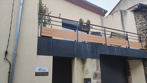 Un edificio de dos pisos con balcón, una puerta de garage negra y una entrada pequeña con un contenedor amarillo.