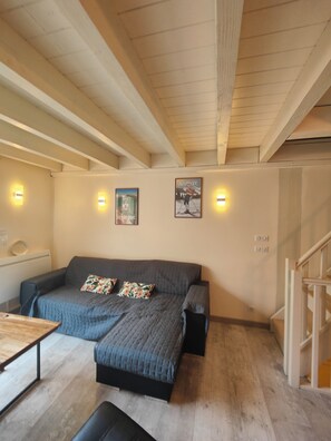 Una habitación acogedora con un sofá gris, dos almohadas, una mesita de madera y una escalera.