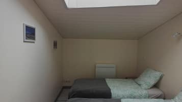 Une petite pièce étroite avec deux lits, une lucarne et un petit tableau accroché au mur.