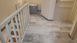 Un pasillo estrecho con piso de madera, barandilla blanca y una puerta a la derecha.