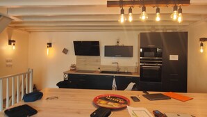Una cocina moderna con una isla de madera, dos taburetes de bar, un horno empotrado y una lámpara colgante.
