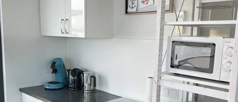A compact kitchen with white cabinets, a microwave, a toaster oven, and a kettle on the counter.