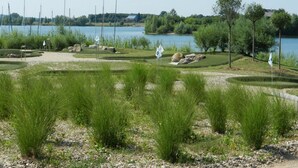 A golf course with bunkers, flags, and a lake in the background. - Hausboot am Xantener Nordsee (Xanten)