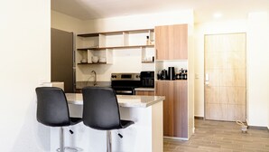 A compact kitchen with a central island, two bar stools, a built-in oven, and a coffee machine.