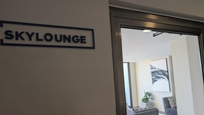 A sign labeled "SKYLounge" on a wall, leading to a modern living area with a grey sofa, a white coffee table, and a plant.